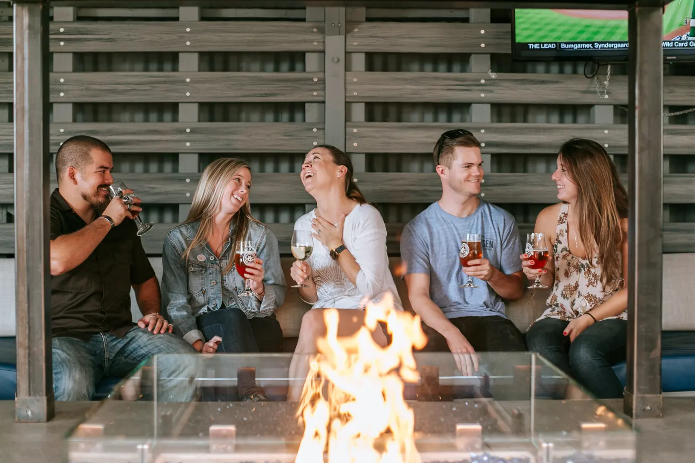 Friends laughing around a fire pit with drinks on the patio