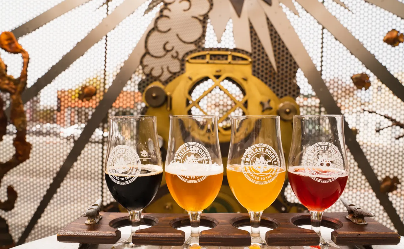 A flight of four Ballast Point beers on a wooden paddle